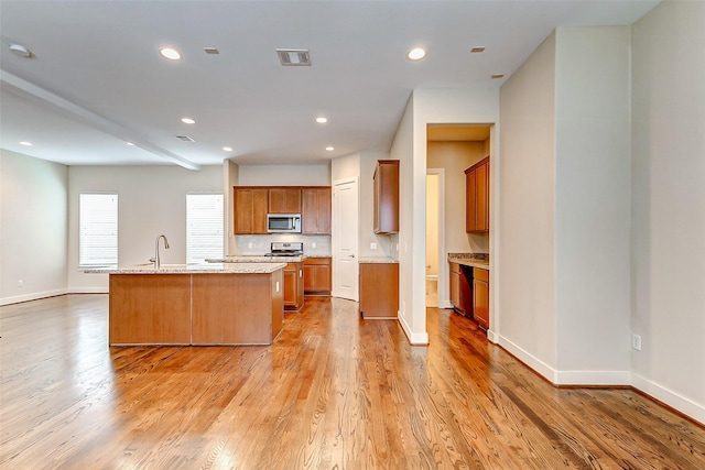 kitchen with visible vents, a center island with sink, brown cabinets, light wood finished floors, and stainless steel appliances
