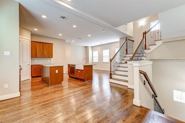 kitchen featuring dishwasher, brown cabinetry, light wood-style flooring, visible vents, and a center island with sink