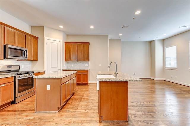 kitchen with stainless steel appliances, a kitchen island with sink, sink, and light wood-type flooring