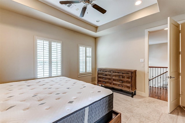 carpeted bedroom with ceiling fan and a tray ceiling