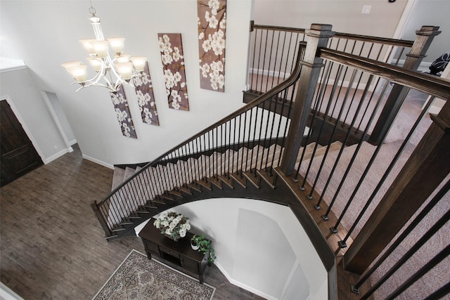 staircase with a towering ceiling, wood-type flooring, and a notable chandelier