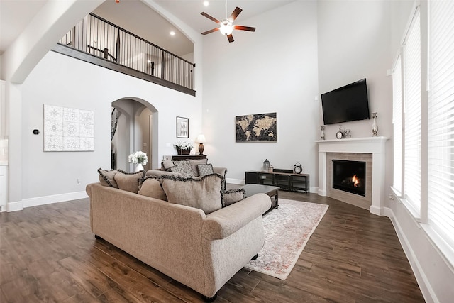 living room featuring ceiling fan, a fireplace, dark hardwood / wood-style floors, and a towering ceiling