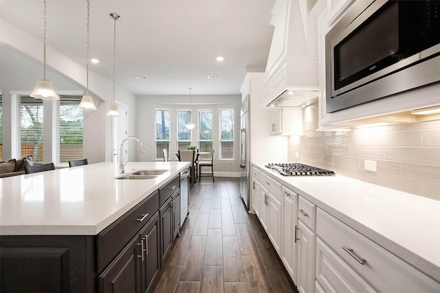 kitchen featuring sink, premium range hood, white cabinetry, stainless steel appliances, and a center island with sink