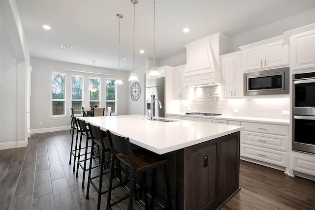 kitchen featuring a spacious island, custom exhaust hood, white cabinetry, built in appliances, and hanging light fixtures