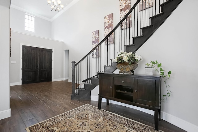 entryway featuring a towering ceiling, ornamental molding, dark hardwood / wood-style flooring, and a notable chandelier