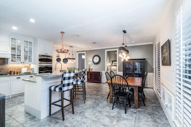 kitchen featuring a kitchen island with sink, a notable chandelier, light stone countertops, white cabinets, and decorative light fixtures