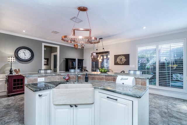 kitchen featuring white cabinetry, sink, decorative light fixtures, and an island with sink