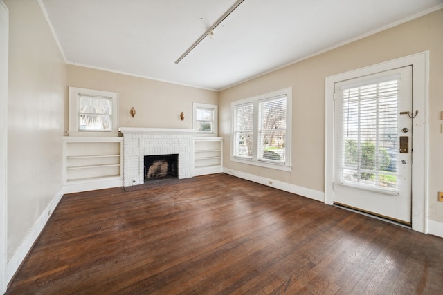 unfurnished living room with dark hardwood / wood-style flooring, crown molding, a brick fireplace, and rail lighting