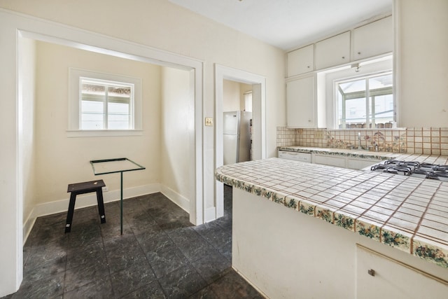 kitchen featuring refrigerator, backsplash, white cabinetry, tile counters, and stainless steel gas cooktop