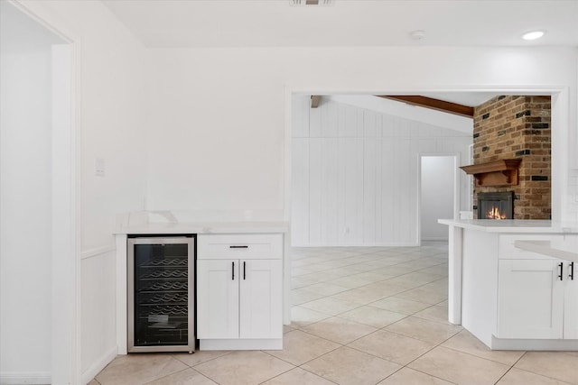 kitchen featuring wine cooler, vaulted ceiling with beams, white cabinetry, a brick fireplace, and light tile patterned floors