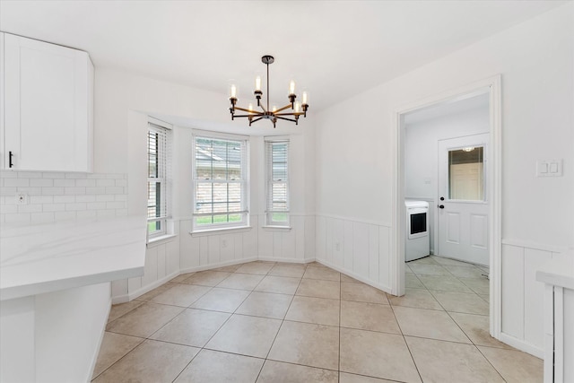 unfurnished dining area featuring an inviting chandelier, washer / clothes dryer, and light tile patterned floors