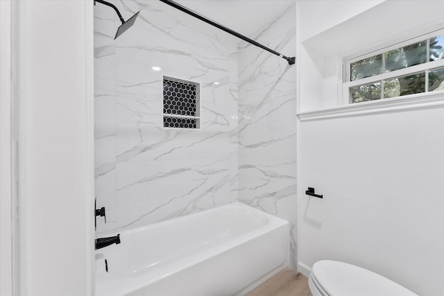 bathroom with hardwood / wood-style flooring, tiled shower / bath, and toilet