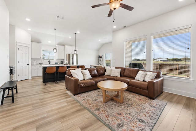 living room with light wood-type flooring, lofted ceiling, sink, and ceiling fan