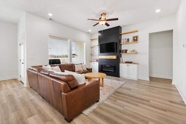 living room with ceiling fan, light hardwood / wood-style flooring, and a large fireplace