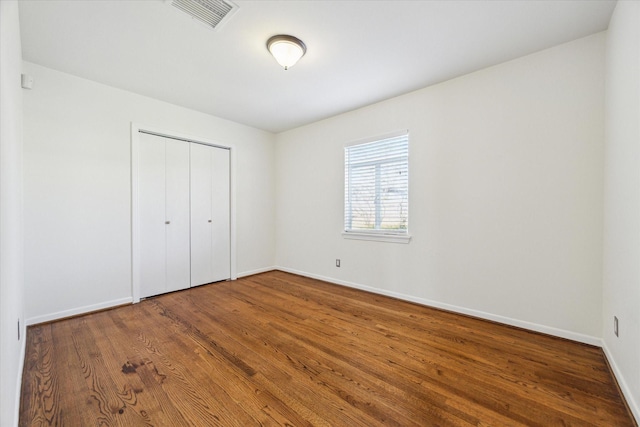 unfurnished bedroom featuring baseboards, visible vents, a closet, and wood finished floors