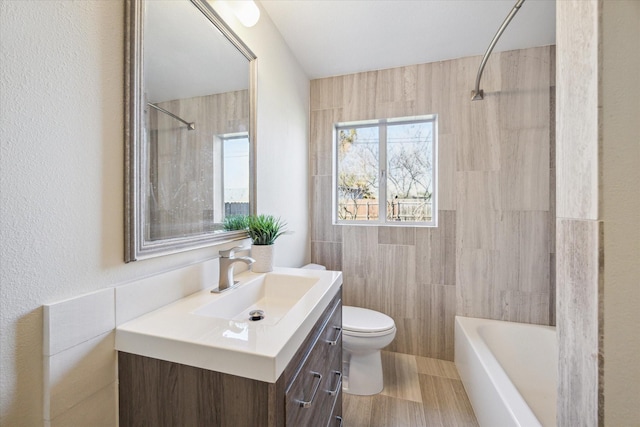 bathroom featuring washtub / shower combination, toilet, vanity, and tile walls