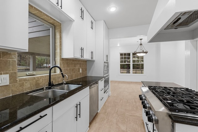 kitchen featuring appliances with stainless steel finishes, pendant lighting, range hood, sink, and white cabinets