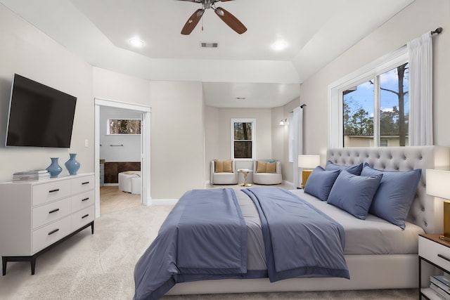 carpeted bedroom featuring a raised ceiling, ensuite bathroom, and ceiling fan