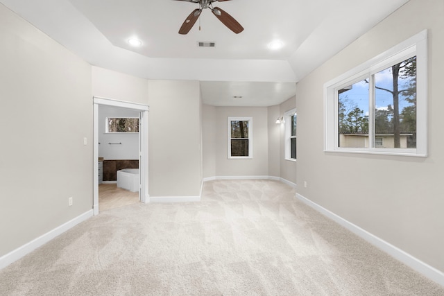 unfurnished bedroom featuring light colored carpet, a tray ceiling, and multiple windows