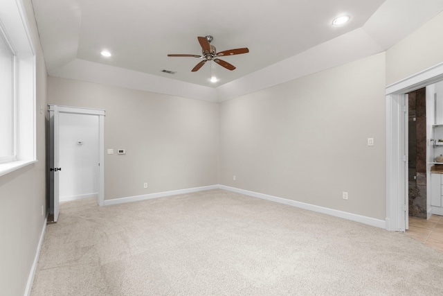 spare room featuring light colored carpet, a raised ceiling, and ceiling fan