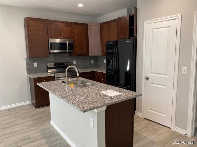 kitchen with stainless steel appliances, tasteful backsplash, light stone countertops, and a center island with sink