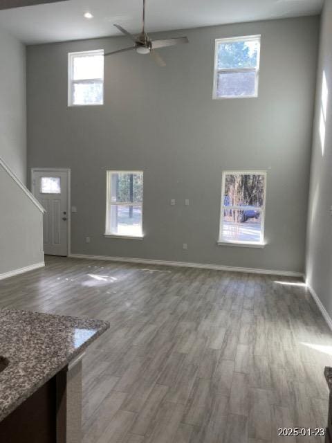 unfurnished living room featuring ceiling fan, dark hardwood / wood-style flooring, and a high ceiling