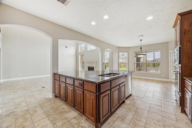 kitchen featuring sink, dark stone countertops, hanging light fixtures, a center island with sink, and stainless steel dishwasher