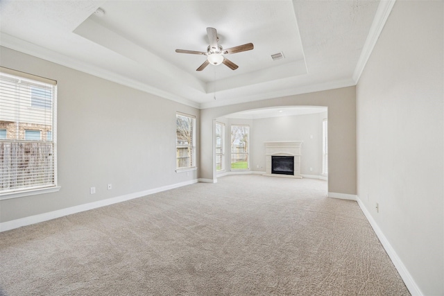 unfurnished living room with ceiling fan, light colored carpet, a tray ceiling, and crown molding