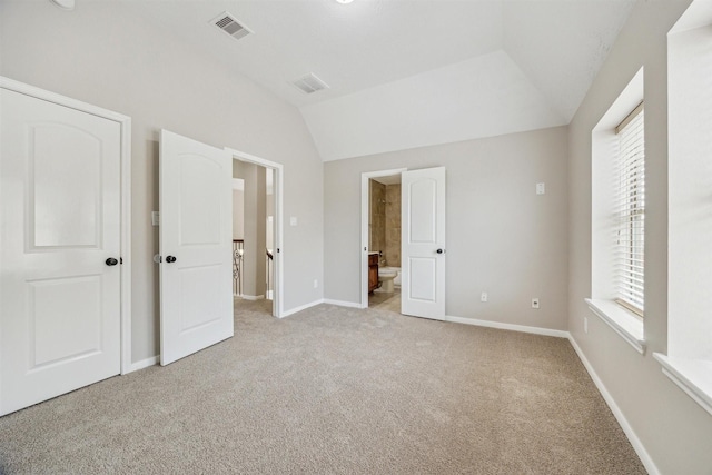 unfurnished bedroom featuring vaulted ceiling, light colored carpet, and ensuite bath