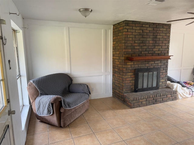 living area with light tile patterned floors, a brick fireplace, and ceiling fan