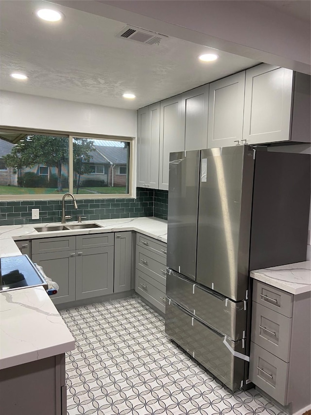 kitchen with sink, gray cabinets, stainless steel refrigerator, light stone counters, and tasteful backsplash