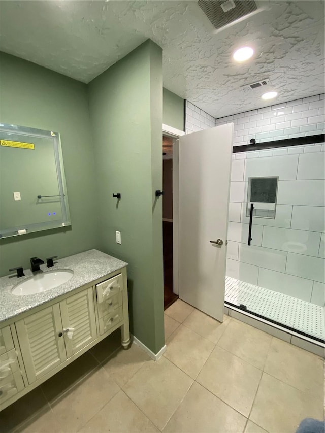 bathroom featuring tile patterned flooring, vanity, tiled shower, and a textured ceiling