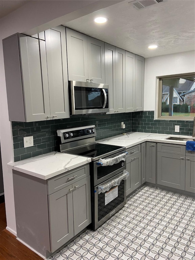 kitchen with gray cabinetry, sink, backsplash, and appliances with stainless steel finishes