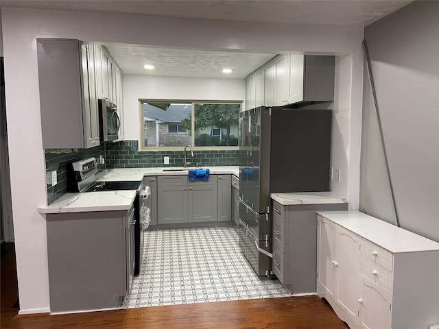 kitchen with gray cabinets, appliances with stainless steel finishes, sink, backsplash, and light wood-type flooring