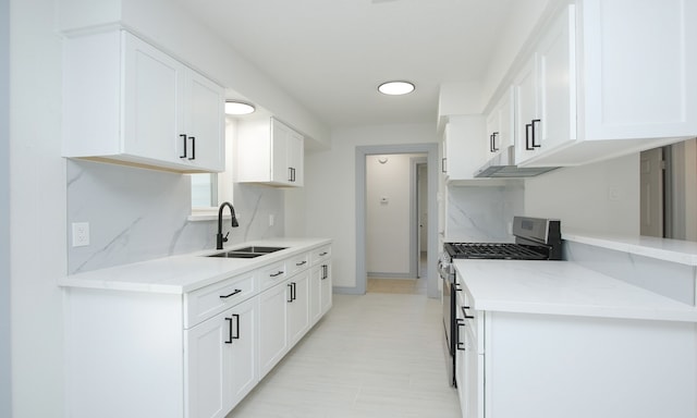 kitchen with tasteful backsplash, gas stove, sink, and white cabinets