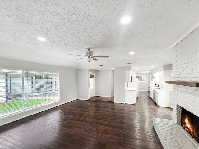 unfurnished living room featuring dark wood-type flooring, ceiling fan, a fireplace, and a textured ceiling