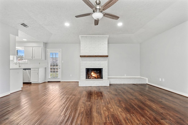 unfurnished living room featuring sink, ceiling fan, dark hardwood / wood-style floors, a fireplace, and a textured ceiling