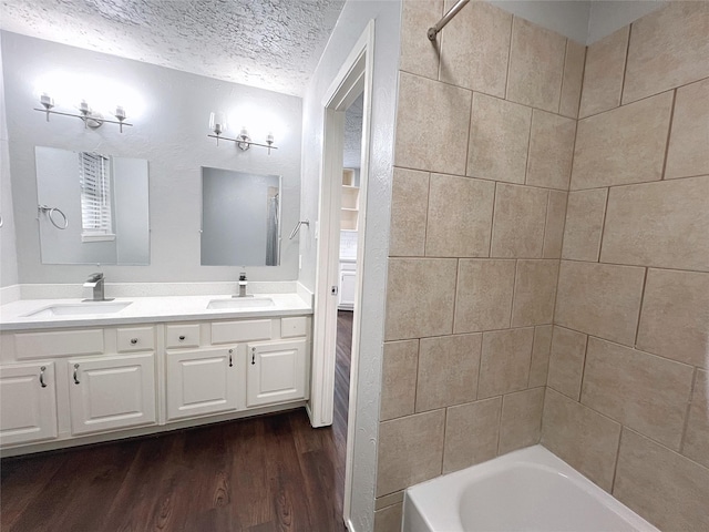 bathroom featuring vanity, tiled shower / bath combo, wood-type flooring, and a textured ceiling