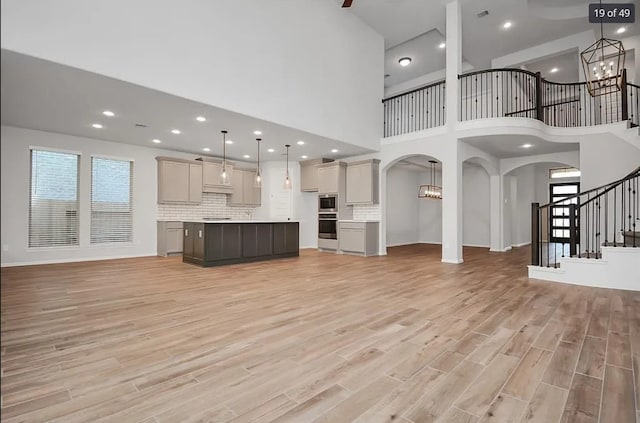 unfurnished living room with a towering ceiling, a chandelier, and light wood-type flooring