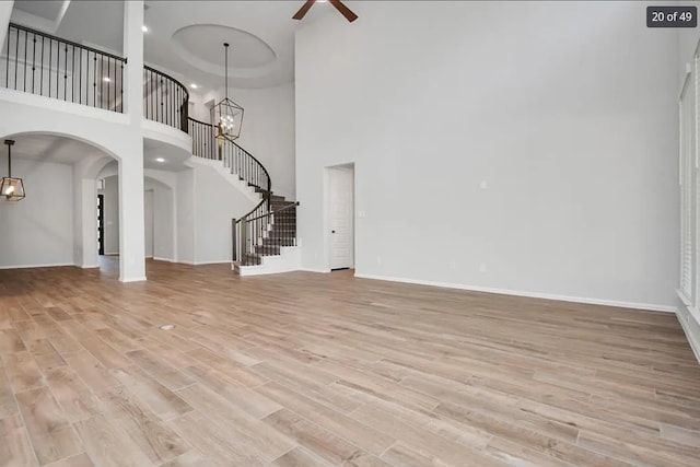 unfurnished living room featuring ceiling fan with notable chandelier and light hardwood / wood-style flooring