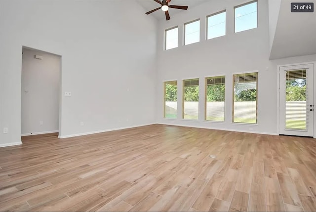 unfurnished living room with a high ceiling, ceiling fan, a wealth of natural light, and light hardwood / wood-style floors