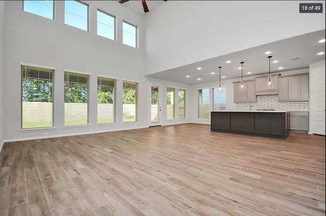 unfurnished living room featuring light hardwood / wood-style floors, ceiling fan, and a high ceiling