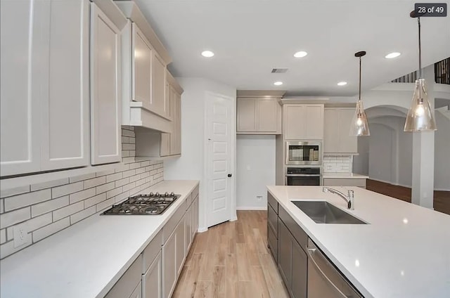 kitchen featuring sink, tasteful backsplash, decorative light fixtures, light wood-type flooring, and stainless steel appliances