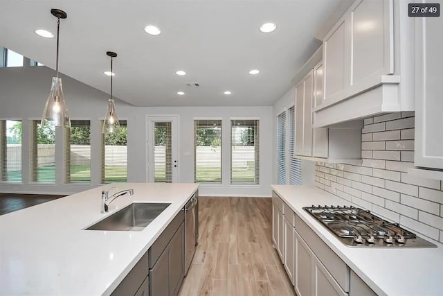 kitchen featuring sink, appliances with stainless steel finishes, light hardwood / wood-style floors, decorative backsplash, and decorative light fixtures