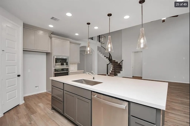 kitchen with sink, hanging light fixtures, a center island with sink, gray cabinets, and stainless steel appliances