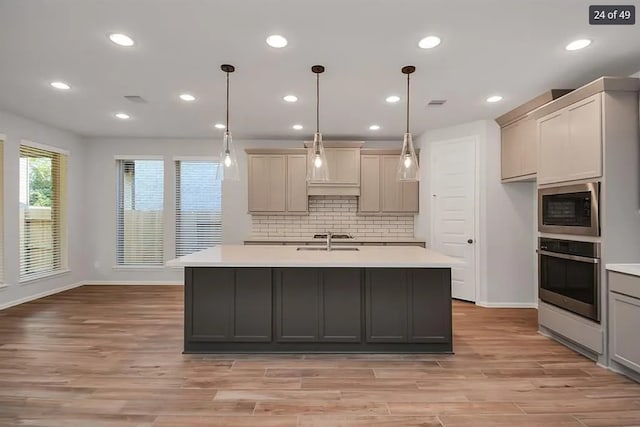 kitchen with built in microwave, sink, stainless steel oven, pendant lighting, and a kitchen island with sink