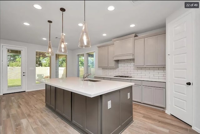 kitchen with pendant lighting, gas cooktop, gray cabinets, and a center island with sink