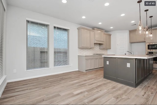 kitchen with gray cabinets, tasteful backsplash, a kitchen island with sink, and decorative light fixtures