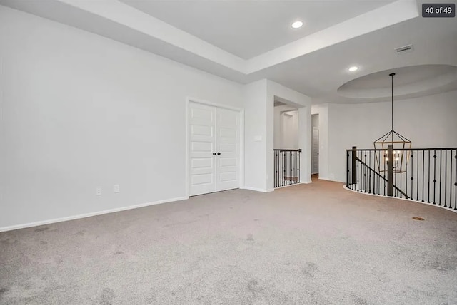 spare room featuring carpet flooring, a tray ceiling, and a notable chandelier