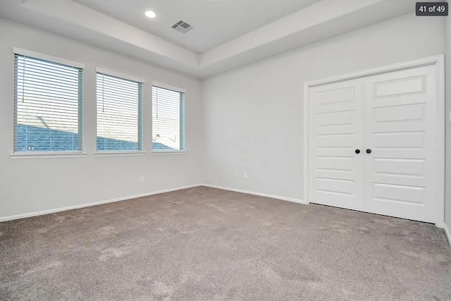 unfurnished bedroom with a raised ceiling, carpet floors, and a closet